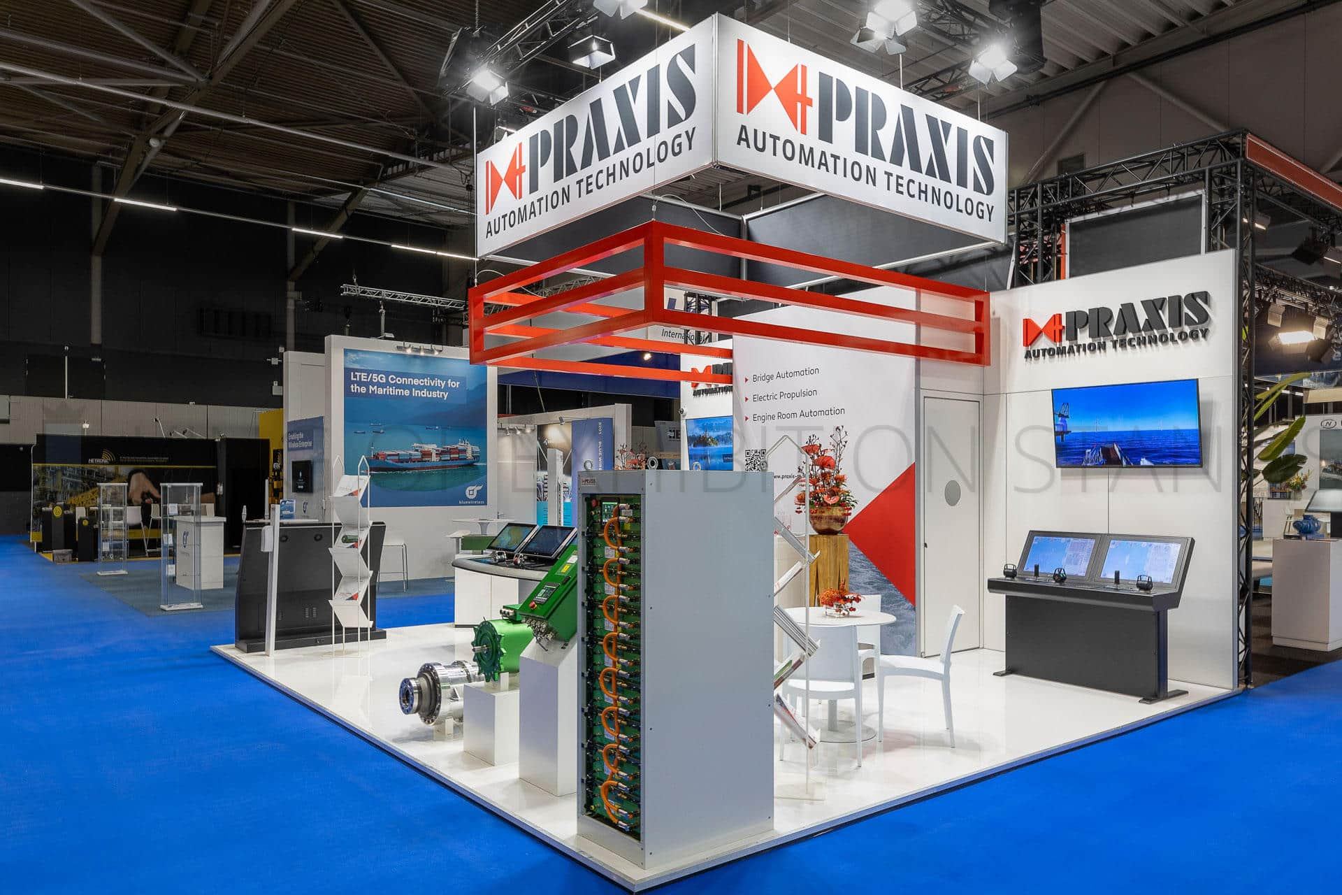 Two-level white stand with a red steel header ring and machinery on plinths